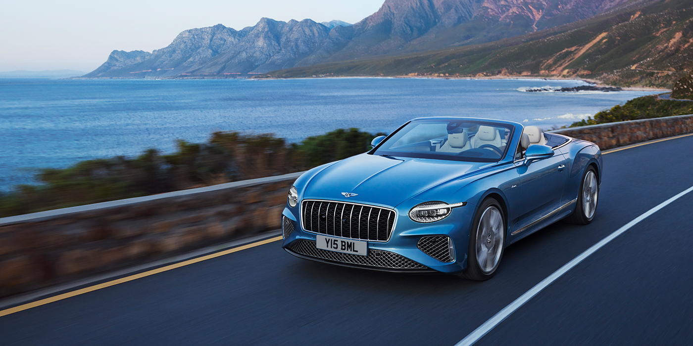 Bentley Geneve New Bentley Continental GTC Azure convertible in Light Windsor blue paint with 22 inch Azure wheels and chrome grill, driving dynamically by the sea