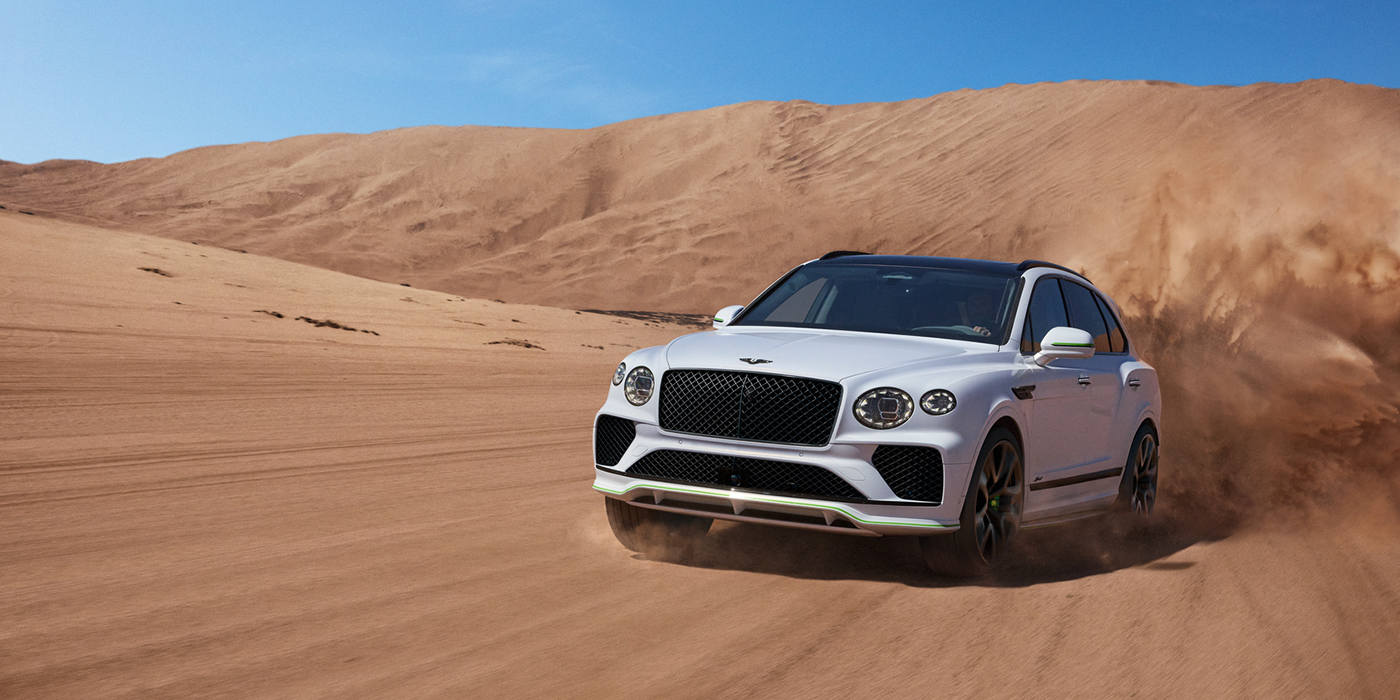 Bentley Geneve Bentley Bentayga Speed SUV front three quarter in Snow Quarts Pearlescent by Mulliner white paint driving dynamically through the desert