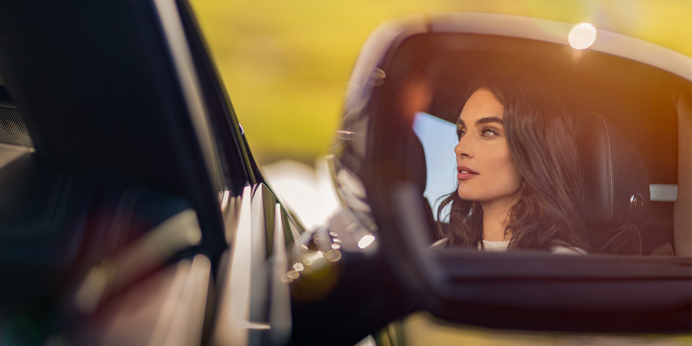 Bentley Geneve profile of dark haired woman's face in mirror of Bentley car in sunlight