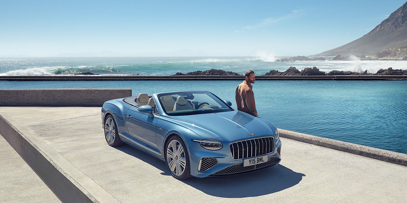 Bentley Geneve New Bentley Continental GTC Azure convertible front view in Light Windsor blue paint with 22 inch ten spoke wheels parked by the sea in the sunshine