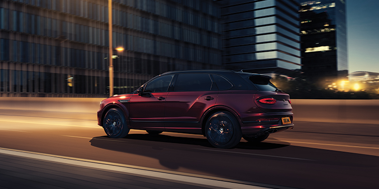 Bentley Geneve Bentley Bentayga Extended Wheelbase Mulliner SUV in Cricket Ball red paint driving dynamically in city at night